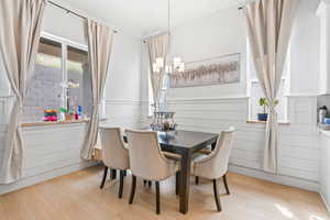 Dining room with light wood-type flooring, a chandelier, and a wainscoted wall
