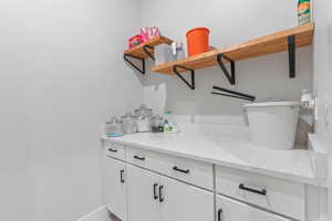 Laundry room featuring white cabinets, open shelves, and light stone countertops