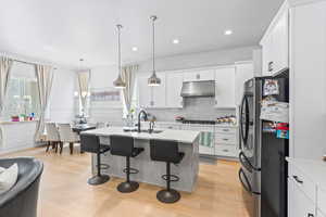 Kitchen with stainless steel appliances, a kitchen breakfast bar, a kitchen island with sink, hanging light fixtures, and light wood-type flooring