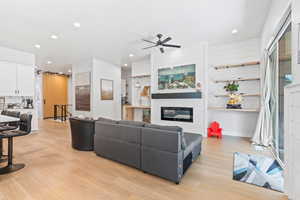 Living area with light wood finished floors, recessed lighting, a glass covered fireplace, and ceiling fan