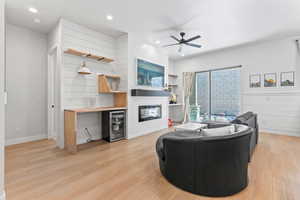 Living room with light wood finished floors, beverage cooler, a glass covered fireplace, recessed lighting, and a ceiling fan