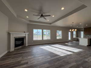 Unfurnished living room with a tray ceiling, a chandelier, recessed lighting, dark wood-type flooring, and a tiled fireplace