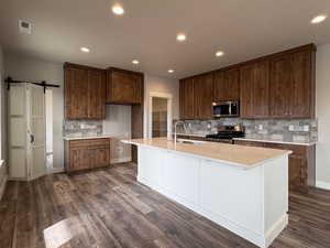Kitchen featuring backsplash, a barn door, stainless steel appliances, an island with sink, and recessed lighting