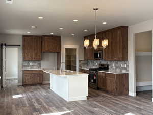 Kitchen with a barn door, decorative backsplash, stainless steel appliances, pendant lighting, and dark wood-style flooring