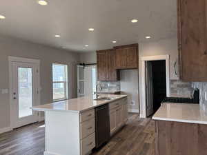 Kitchen with a barn door, light stone counters, appliances with stainless steel finishes, recessed lighting, and dark wood-style flooring