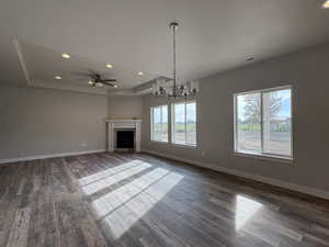 Unfurnished living room with a tray ceiling, recessed lighting, a chandelier, a fireplace, and dark wood-style flooring