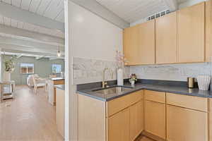 Kitchen featuring light brown cabinets, beam ceiling, open floor plan, backsplash, and light wood-style flooring