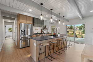 Kitchen featuring stainless steel appliances, beamed ceiling, a kitchen bar, an island with sink, and backsplash