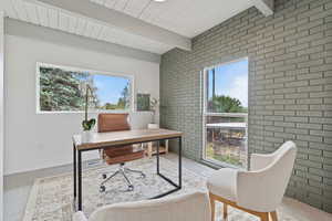 Office area with brick wall, carpet flooring, and a wooden ceiling with exposed beams