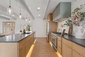 Kitchen featuring dark countertops, a large island, pendant lighting, appliances with stainless steel finishes, and light wood-type flooring