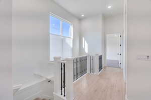 Hallway featuring light wood-style flooring, an upstairs landing, and recessed lighting
