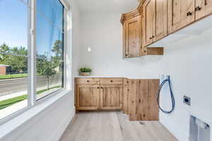 Laundry room with cabinets, counter top, expansive windows for natural light, electric dryer hookup, and light wood finished floors