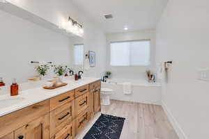 Full bath with double vanity, light wood-style flooring, and a jetted tub
