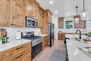 Kitchen with stainless steel appliances, decorative backsplash, quartz countertops, decorative light fixtures, and light wood-style flooring