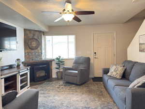 Living area with a textured ceiling, a ceiling fan, and a wood stove