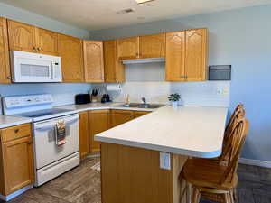 Kitchen with white appliances, a kitchen breakfast bar, light countertops, a peninsula, and decorative backsplash