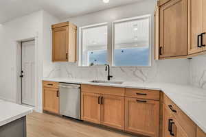 Kitchen featuring dishwasher, light stone countertops, light wood-style floors, and tasteful backsplash