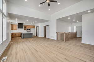 Unfurnished living room featuring a barn door, light wood-type flooring, recessed lighting, and a ceiling fan
