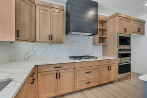 Kitchen with light stone countertops, premium range hood, decorative backsplash, open shelves, and light wood-type flooring