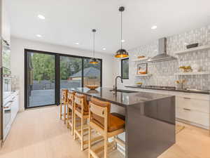 Gourmet kitchen featuring tasteful backsplash, open shelves, light wood-type flooring, decorative light fixtures, and recessed lighting