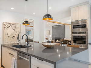 Kitchen with a large fireplace, modern cabinets, stainless steel appliances, hanging light fixtures, and recessed lighting