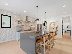 Gourmet kitchen with open shelves, a kitchen bar, an island with sink, hanging light fixtures, and recessed lighting