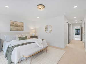 Bedroom with recessed lighting, light carpet, and a barn door