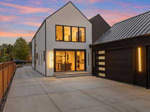 Rear view of property at dusk featuring a standing seam roof, concrete driveway, a metal roof, and an attached garage