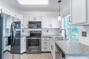 Kitchen featuring stainless steel appliances, white cabinetry, pendant lighting, and light countertops