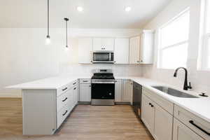 Kitchen with stainless steel appliances, a peninsula, light wood-style floors, and pendant lighting