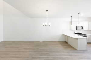 Kitchen featuring stainless steel appliances, white cabinetry, light wood-type flooring, suspended lighting, and a peninsula