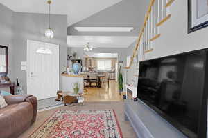 Living room featuring light colored carpet, stairs, a ceiling fan, and a high ceiling