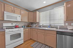 Kitchen with white appliances, light brown cabinetry, crown molding, light wood-style flooring, and light countertops