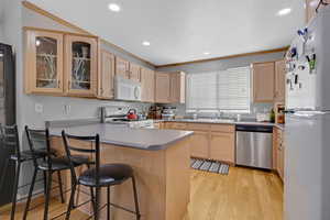 Kitchen with white appliances, glass insert cabinets, light brown cabinets, light wood finished floors, and crown molding