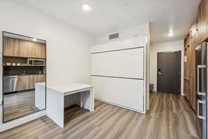 Kitchen featuring modern cabinets, brown cabinetry, appliances with stainless steel finishes, light wood-type flooring, and recessed lighting