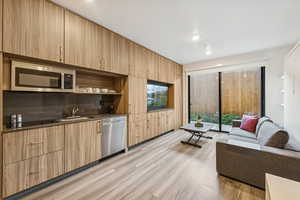 Kitchen with open shelves, stainless steel appliances, light wood finished floors, modern cabinets, and light brown cabinets