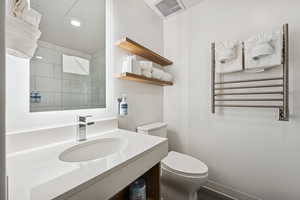 Bathroom with a towel warming rack, radiator, vanity, and a tile shower