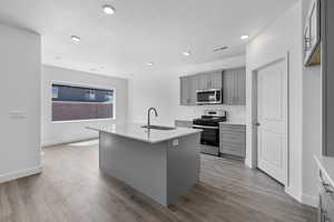 Kitchen featuring gray cabinets, stainless steel appliances, a center island with sink, light wood finished floors, and recessed lighting