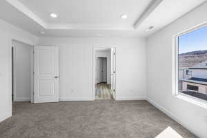Unfurnished bedroom featuring a tray ceiling, light carpet, recessed lighting, and a mountain view