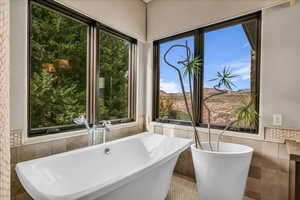 Full bath with tile walls, a wainscoted wall, a soaking tub, a mountain view, and tile patterned floors