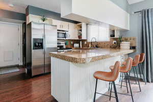 Kitchen featuring stainless steel appliances, a breakfast bar area, a peninsula, dark wood-type flooring, and white cabinetry