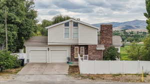 View of front of home with a garage, a chimney, concrete driveway, brick siding, and a mountain view