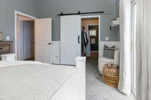 Bedroom featuring carpet flooring, a barn door, a spacious closet, and a wainscoted wall