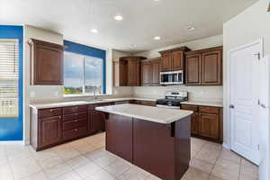 Kitchen featuring stainless steel appliances, light countertops, a kitchen bar, a textured ceiling, and a center island