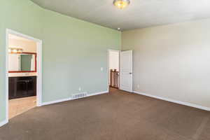 Unfurnished bedroom with carpet floors, ensuite bath, and a textured ceiling