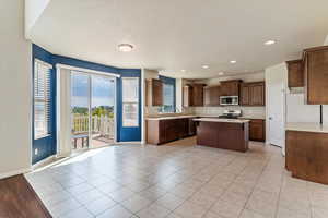 Kitchen featuring light countertops, stainless steel appliances, light tile patterned floors, a kitchen island, and a textured ceiling
