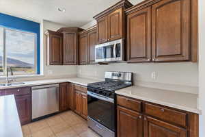 Kitchen with appliances with stainless steel finishes, light tile patterned flooring, and a textured ceiling
