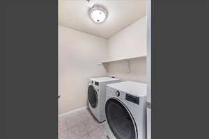 Washroom with a textured ceiling, light tile patterned flooring, and washing machine and dryer