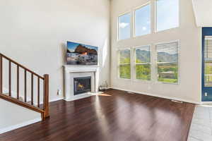 Unfurnished living room with a tiled fireplace, wood finished floors, stairs, and a towering ceiling