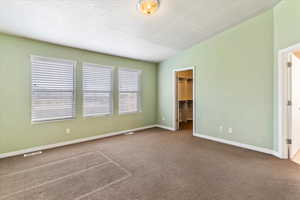Unfurnished bedroom featuring a textured ceiling, carpet floors, a walk in closet, and vaulted ceiling